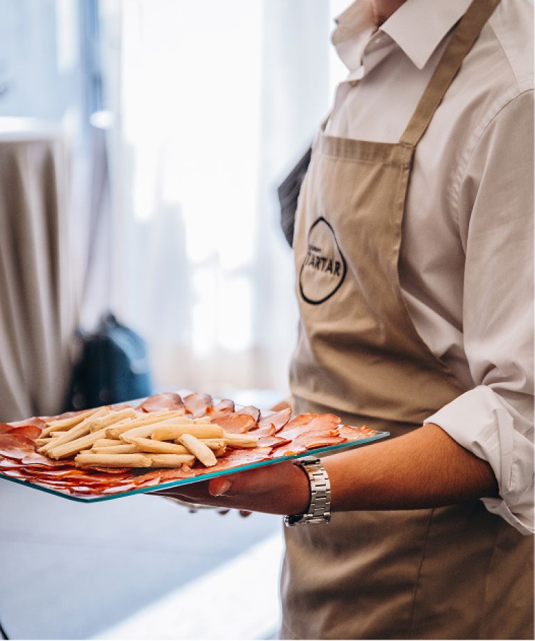 Camarero del Grupo Tartar sirviendo una bandeja con jamón ibérico y picos en evento gourmet