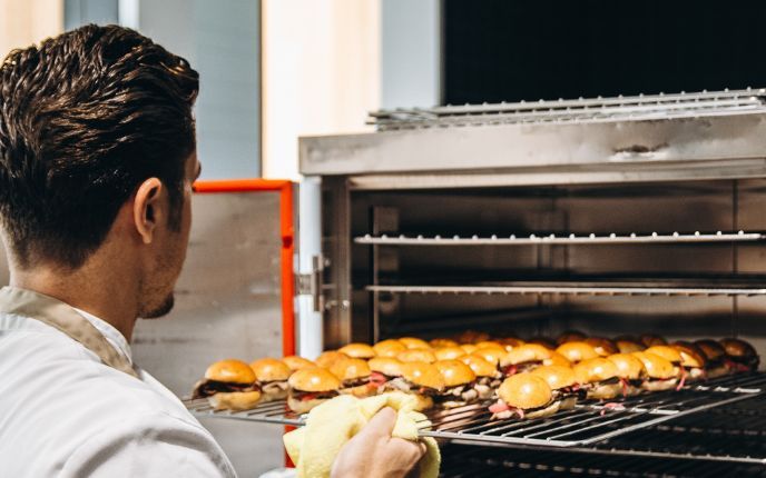 Cocinero de Grupo Tartar sacando bandeja de mini hamburguesas recién horneadas para catering de eventos